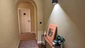 Un pasillo con piso de madera, un banco con una planta y una lámpara de pared.