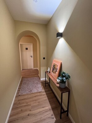 A hallway with a wooden floor, a bench with a plant, and a wall-mounted light fixture.