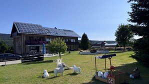 Un edificio con techo de paneles solares, un área de juegos y una zona vallada con esculturas de ovejas.