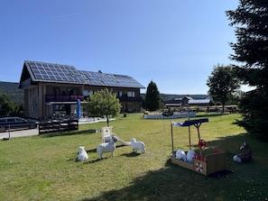 A building with a solar panel roof, a playground, and a fenced area with sheep sculptures.