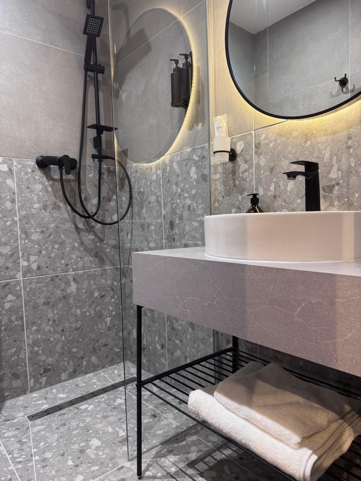 A modern bathroom with a shower, a sink, and a towel rack.