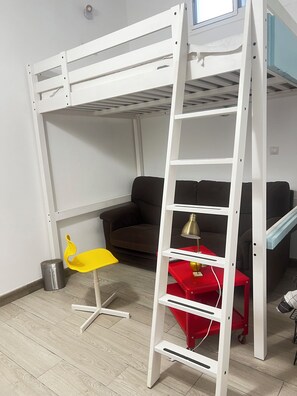 A bunk bed with a ladder, a red side table with a lamp, a yellow chair, and a brown sofa in a room with wooden flooring. - Las Palmas Castillo Albrit Community Center (Las Palmas de Gran Canaria)