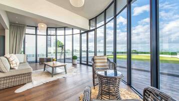 A spacious living area with a large window, a sofa, a coffee table, and a wicker chair.