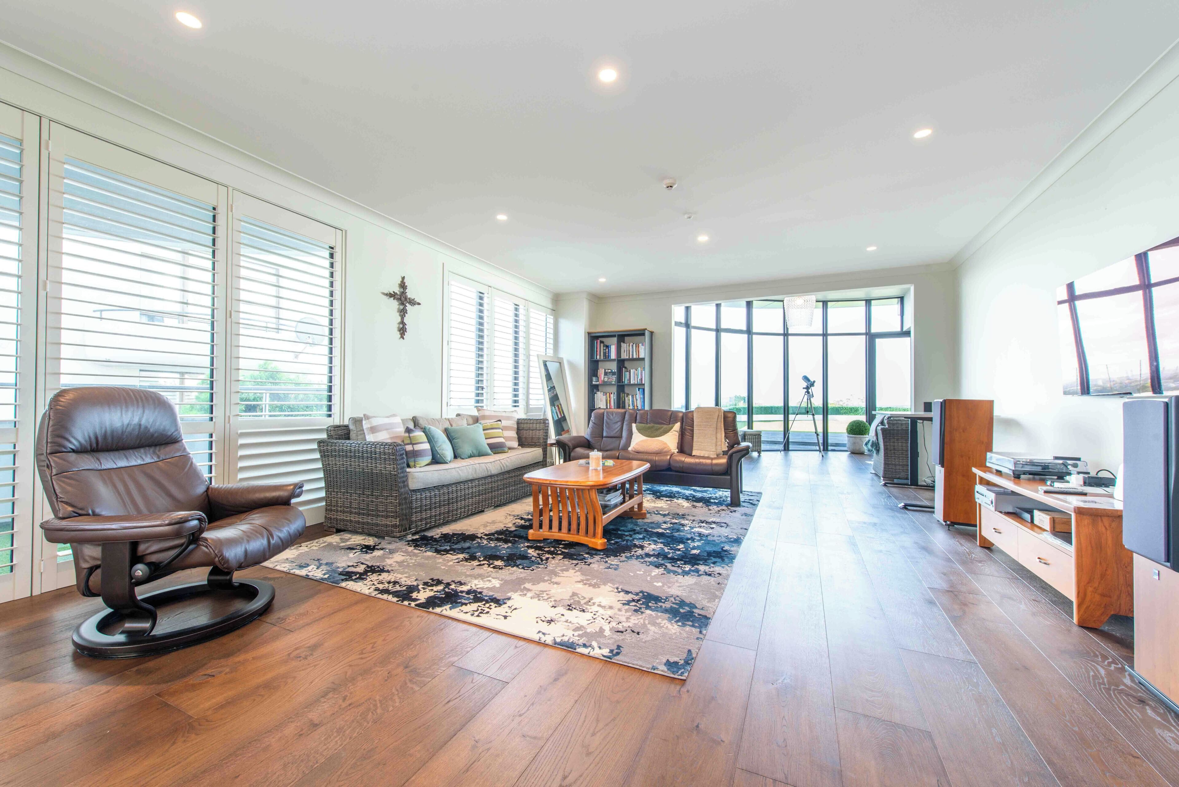 A spacious living room with a leather chair, a sofa, a coffee table, and a bookshelf.