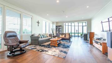 A spacious living room with a leather chair, a sofa, a coffee table, and a bookshelf.