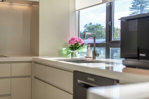 A modern kitchen with a stainless steel sink, a faucet, and a window with a view of trees. - Luxury 3BR Apartment with Stunning Views | Remuera (Auckland)