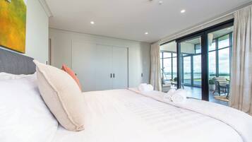 A modern hotel room with a large bed, a view of the outdoors through a sliding glass door, and a painting on the wall.