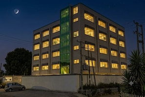 A multi-story building with illuminated windows at night, a visible car in the foreground, and a crescent moon in the sky. - Big Z Hote (Addis Ababa)