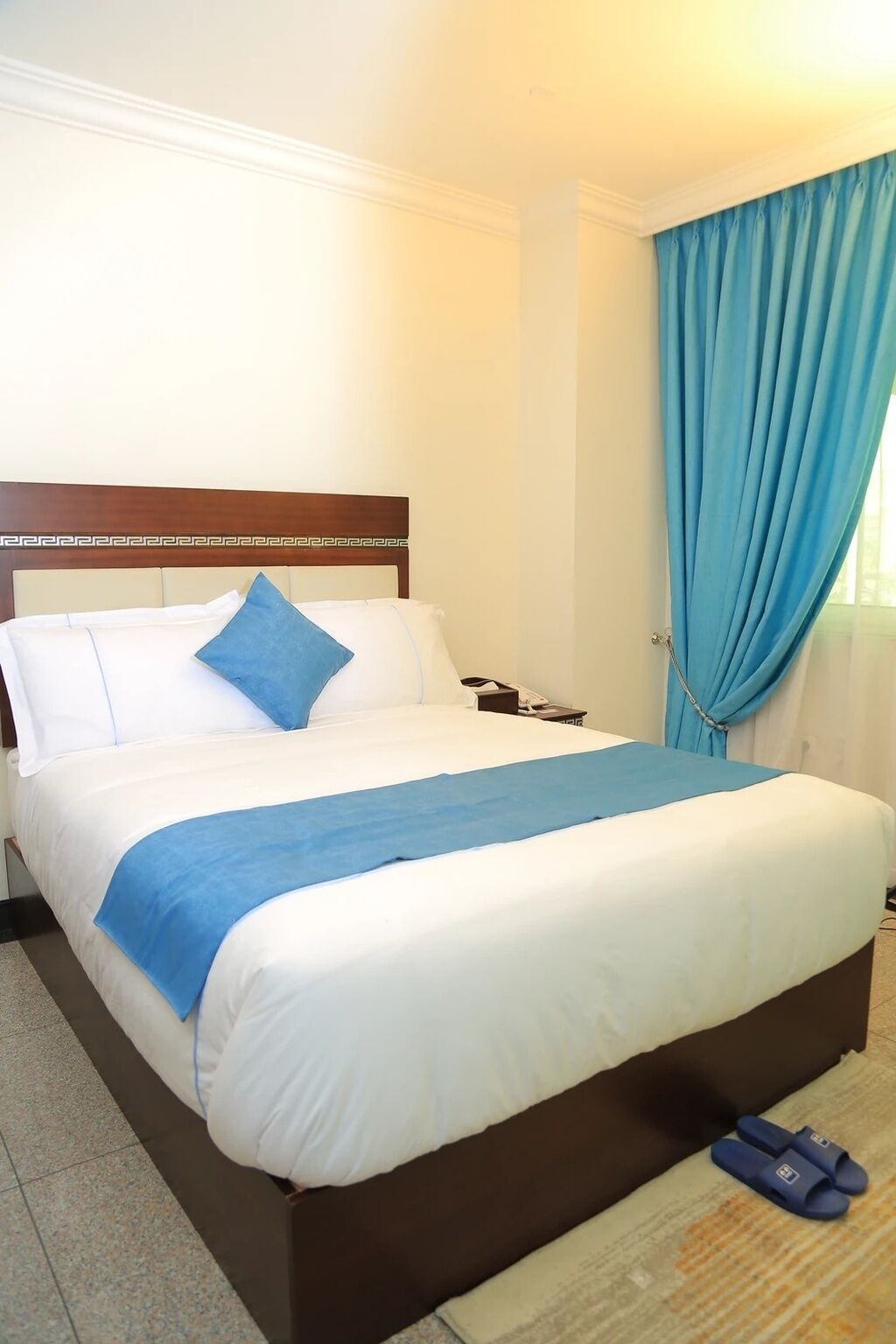 A hotel room with a bed, a nightstand, a telephone, and a pair of slippers.