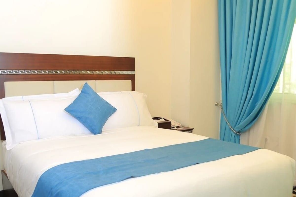A hotel room with a bed, a nightstand, a telephone, and a pair of slippers.