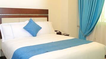 A hotel room with a bed, a nightstand, a telephone, and a pair of slippers.