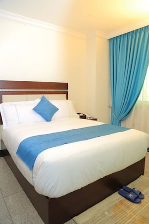 A hotel room with a bed, a nightstand, a telephone, and a pair of slippers. - Big Z Hote (Addis Ababa)