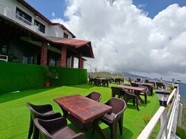 An outdoor seating area with tables and chairs, a green lawn, and a building with a red roof in the background.
