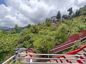 A view of a hillside with a red staircase leading up, surrounded by lush greenery and a building in the background.