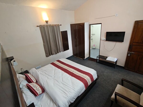 A hotel room with a bed, a bedside table, a TV, a wardrobe, and a shower area.