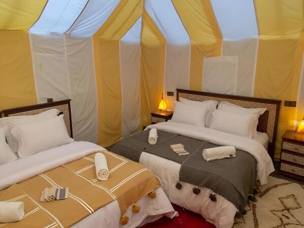 A tent-style room with two beds, each with a headboard, bedside tables, and lamps.