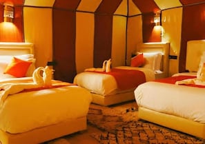 Habitación de hotel con tres camas dispuestas en fila, cada una con una almohada roja y una toalla blanca.
