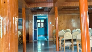 A wooden interior with a tiled floor, a corridor leading to a room with a blue door, and several chairs arranged in the foreground. - Adhaan Guest House (Srinagar)