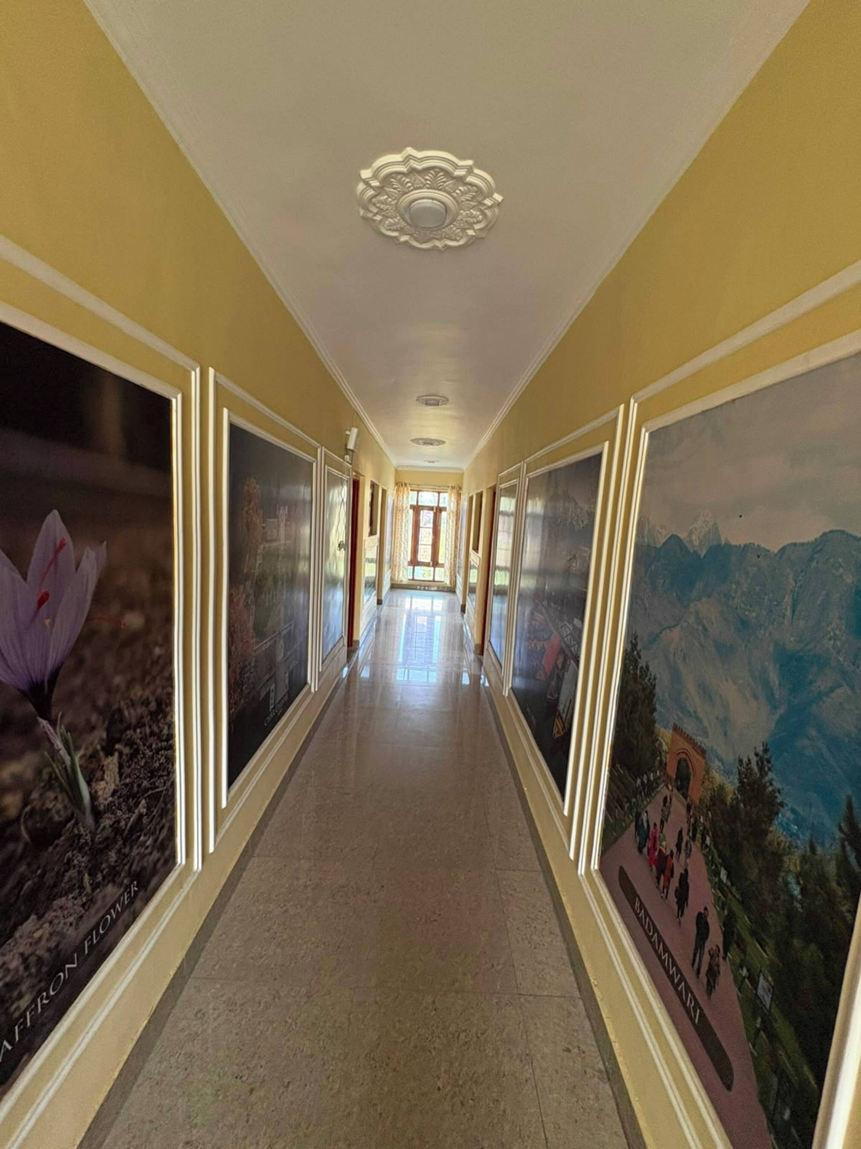 A hallway with framed artwork on the walls, a polished floor, and a ceiling with a decorative light fixture.