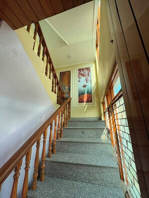 Una escalera con barandillas de madera, suelo de granito y una puerta con un cuadro enmarcado.