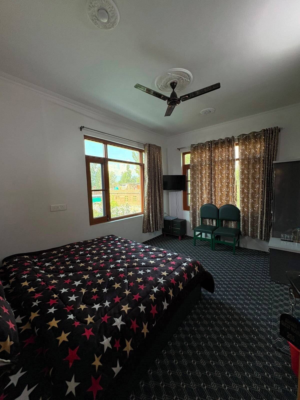 A hotel room with a bed, a ceiling fan, a TV, and a desk with chairs.