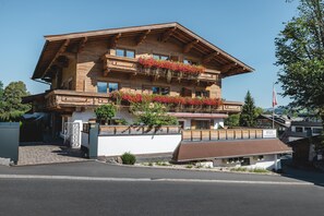 A wooden multi-story building with balconies adorned with flowers, a white facade, and a clear sky. - Mocking Ferienappartements (Kitzbühel)
