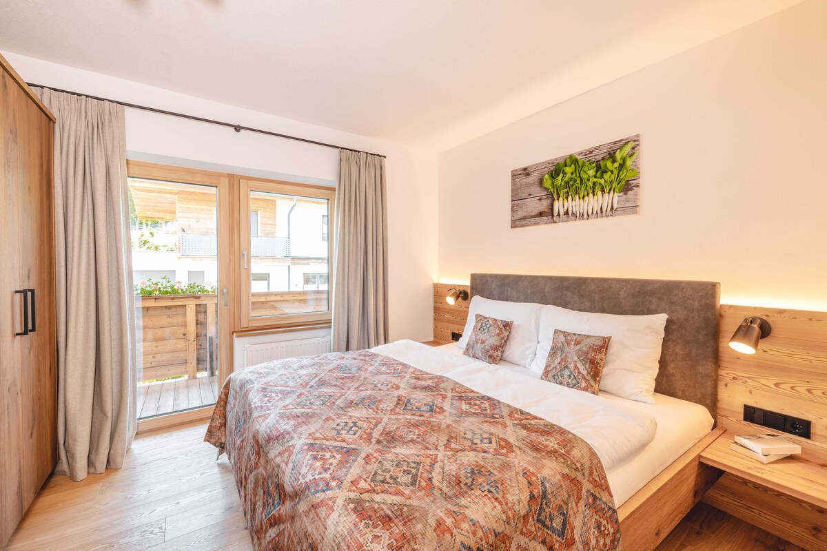 A bedroom with a bed, a window with curtains, a wall-mounted light, and a wooden headboard.