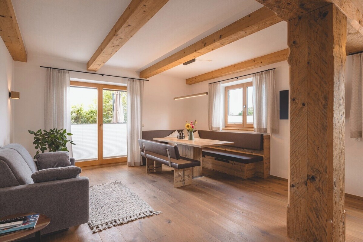 A cozy room with a wooden ceiling, a sofa, a dining table with benches, and large windows.