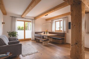 A cozy room with a wooden ceiling, a sofa, a dining table with benches, and large windows. - Mocking Ferienappartements (Kitzbühel)