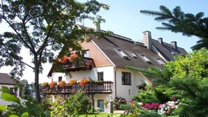 A two-story house with a sloped roof, a balcony with flower boxes, and a well-maintained garden. - Apartment 'FeWo "Ober Stube"' with Shared Garden and Wi-Fi (Marienberg)