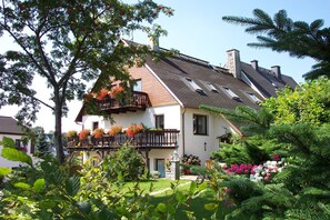 Ein zweistöckiges Haus mit einem geneigten Dach, einem Balkon mit Blumenkästen und einem gepflegten Garten.