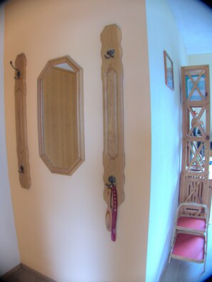Ein Zimmer mit einem hölzernen Kleiderständer, einem Spiegel und einem Korbstuhl mit rosa Kissen.
