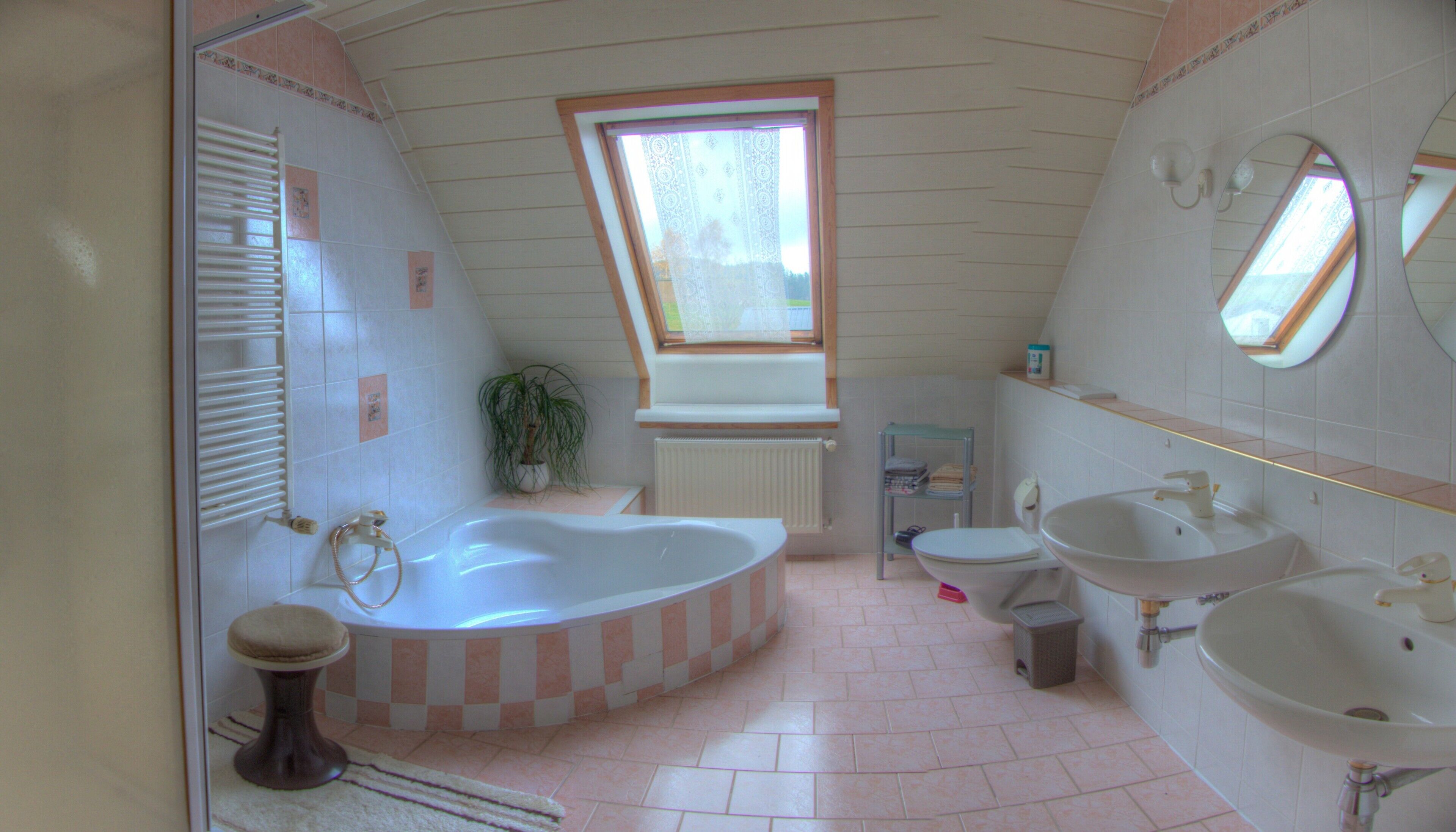 Een badkamer met een bad, twee wastafels, een toilet, een raam en een radiator.