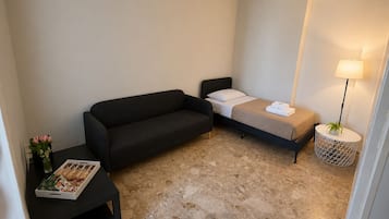 Une chambre d’hôtel de taille réduite, comprenant un lit, un canapé, une petite table avec un magazine et une lampe.