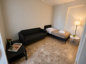 Une chambre d’hôtel de taille réduite, comprenant un lit, un canapé, une petite table avec un magazine et une lampe.