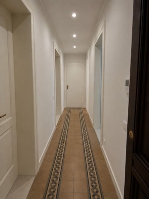 A hallway with white walls, a patterned carpet, and a door at the end.