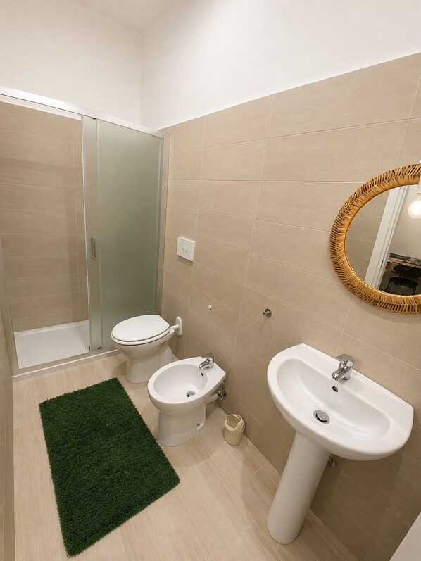 A bathroom with a shower, toilet, bidet, sink, and a mirror with a decorative frame.