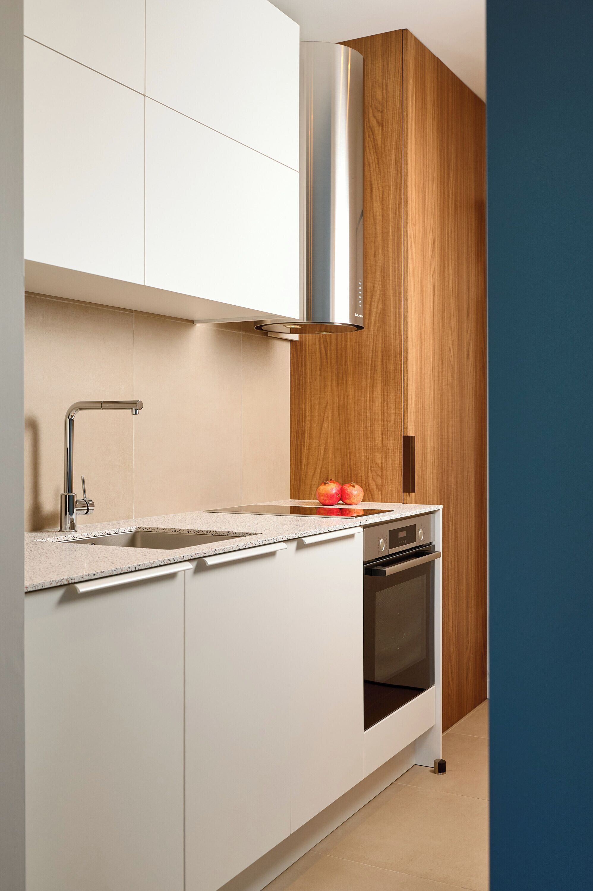 Una cocina moderna con armarios blancos, un grifo de acero inoxidable, horno empotrado y una pared de acento de madera.