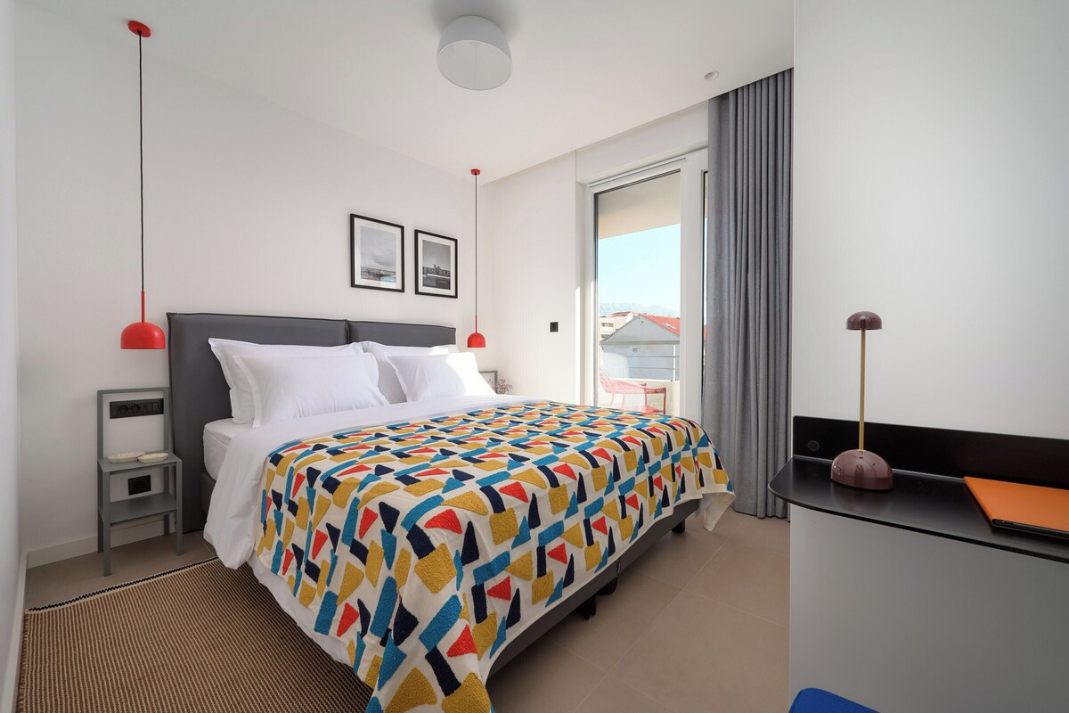 A hotel room with a bed, bedside tables, a desk, and a chair.