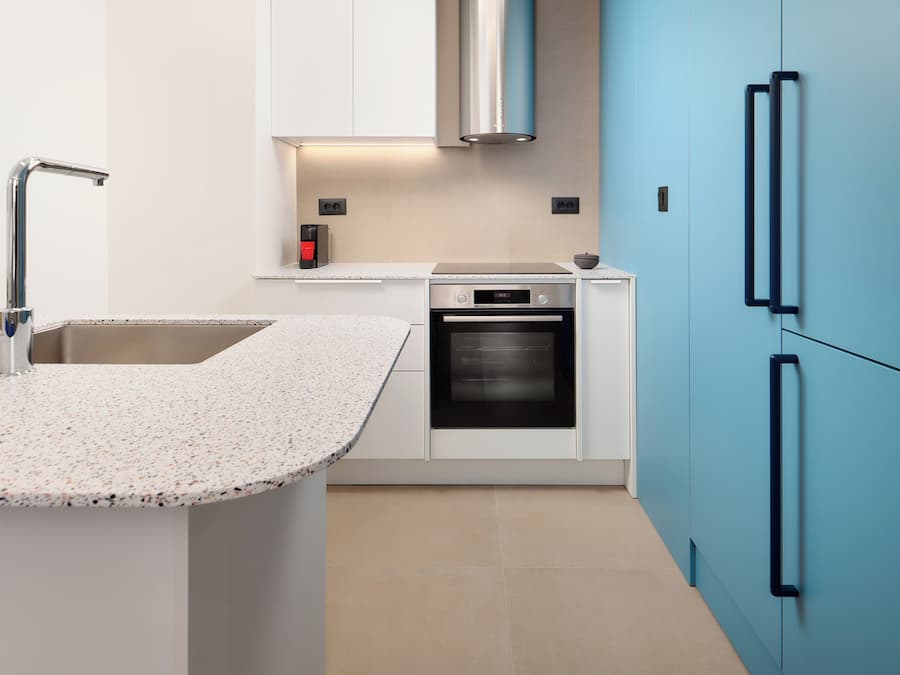 A modern kitchen with a granite countertop, stainless steel appliances, and blue cabinetry.