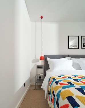 A hotel room with a bed, a bedside table, a lamp, and a wall-mounted light fixture.