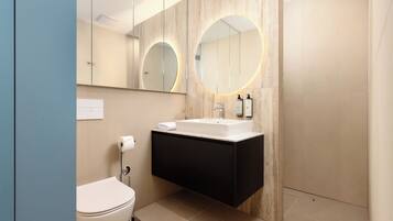 Un baño moderno con inodoro, lavabo y espejo con luces circulares.