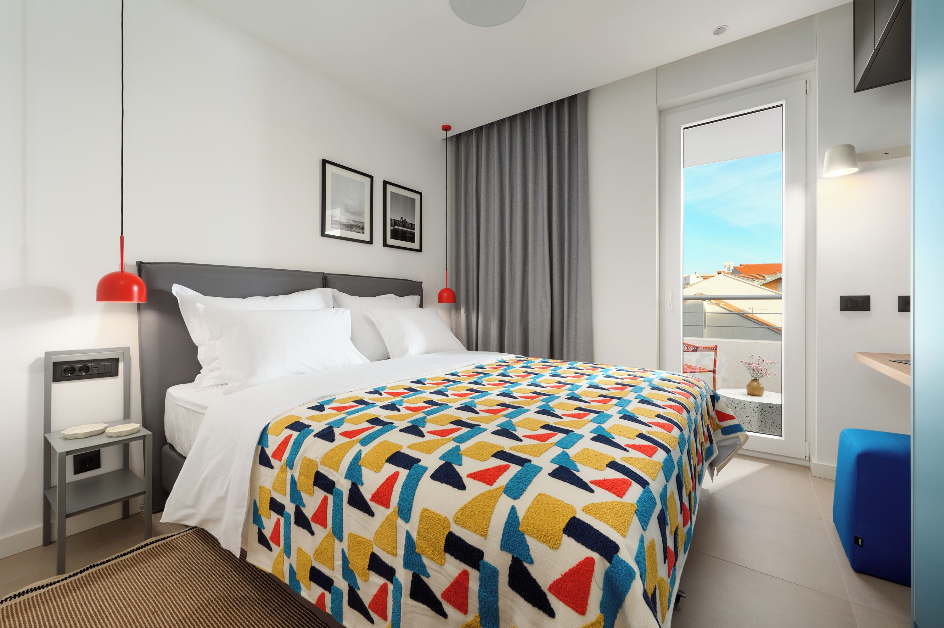 A modern hotel room with a bed, bedside tables, a window with a view, and a blue chair.