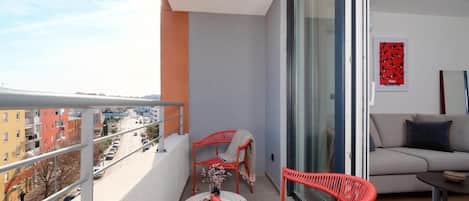 A balcony with red wicker chairs, a small table with a vase, and a sofa.