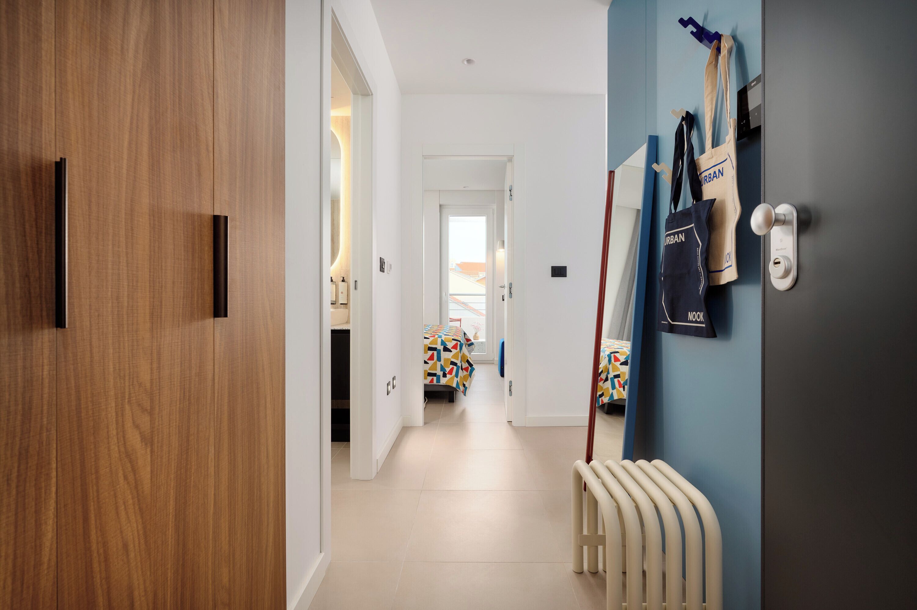 A hallway with a wooden door, a radiator, and a bed with a colorful geometric-patterned bedspread.
