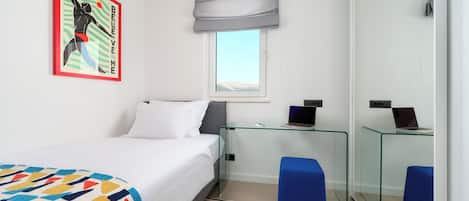 A bedroom with a bed, a glass desk, a laptop, a blue chair, and a window with a view.