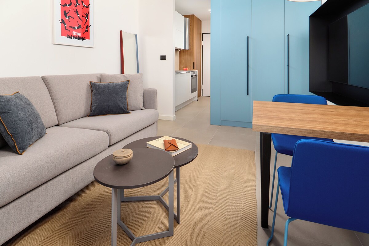 A modern living room with a sofa, a small round table, and a blue chair.