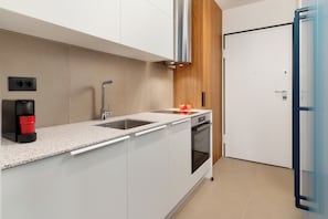 Una cocina moderna con armarios blancos, un lavamanos de acero inoxidable, un horno empotrado y una pared de acento de madera.