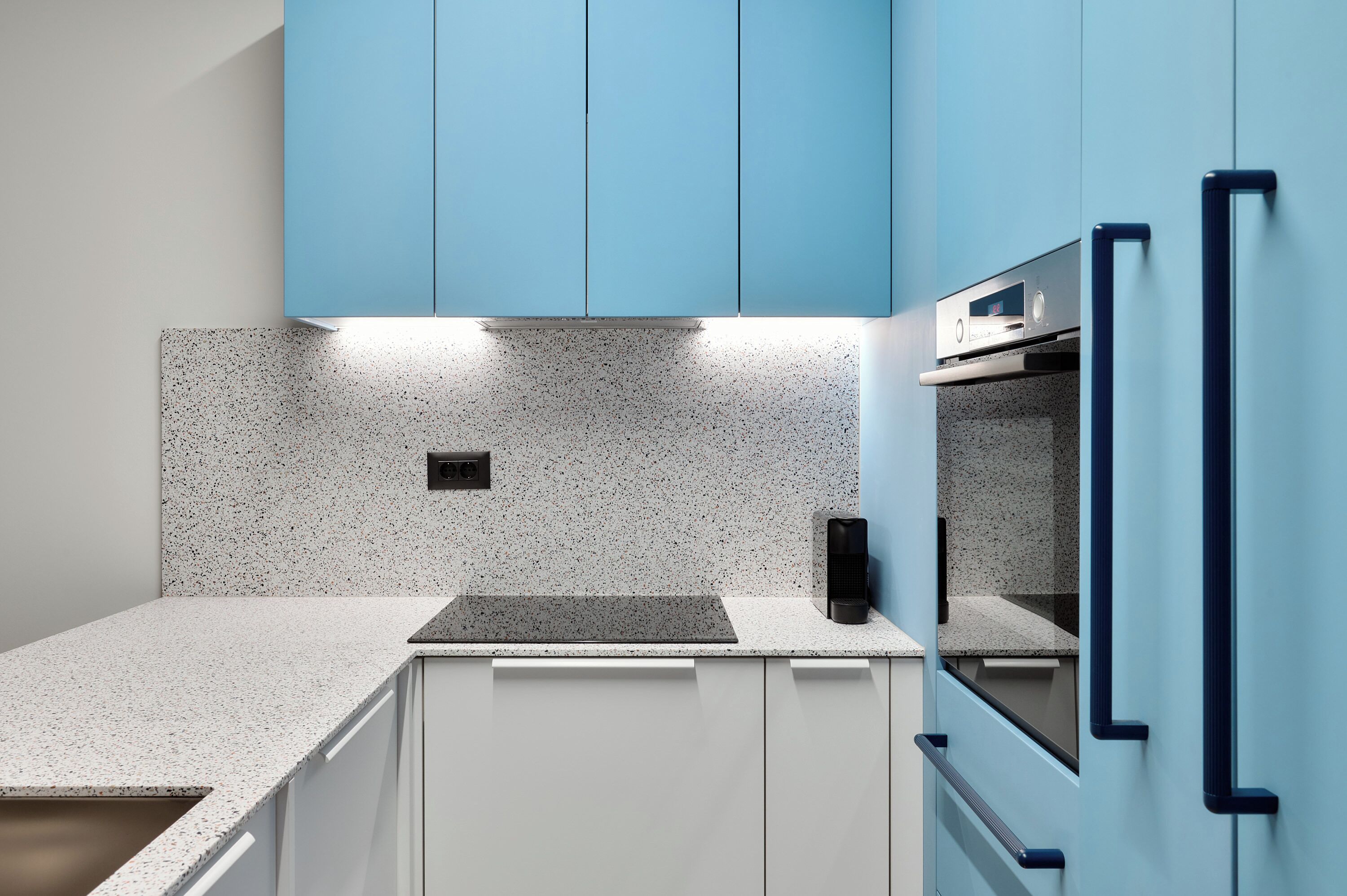 A modern kitchen with a speckled backsplash, white cabinets, and blue upper cabinets.