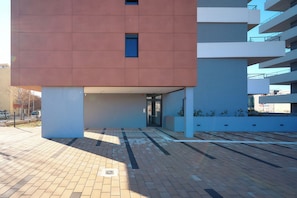 Un edificio moderno con fachada plana, una entrada pequeña y un estacionamiento con pavimento estampado.